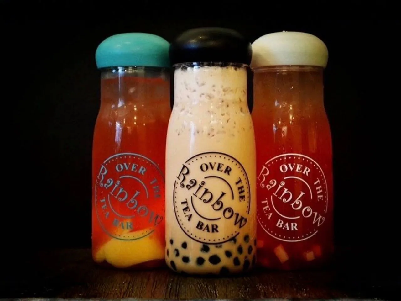 Three bottled fruit and milk bubble tea drinks with colorful lids at Over The Rainbow Tea Bar, a Tea House in Renton