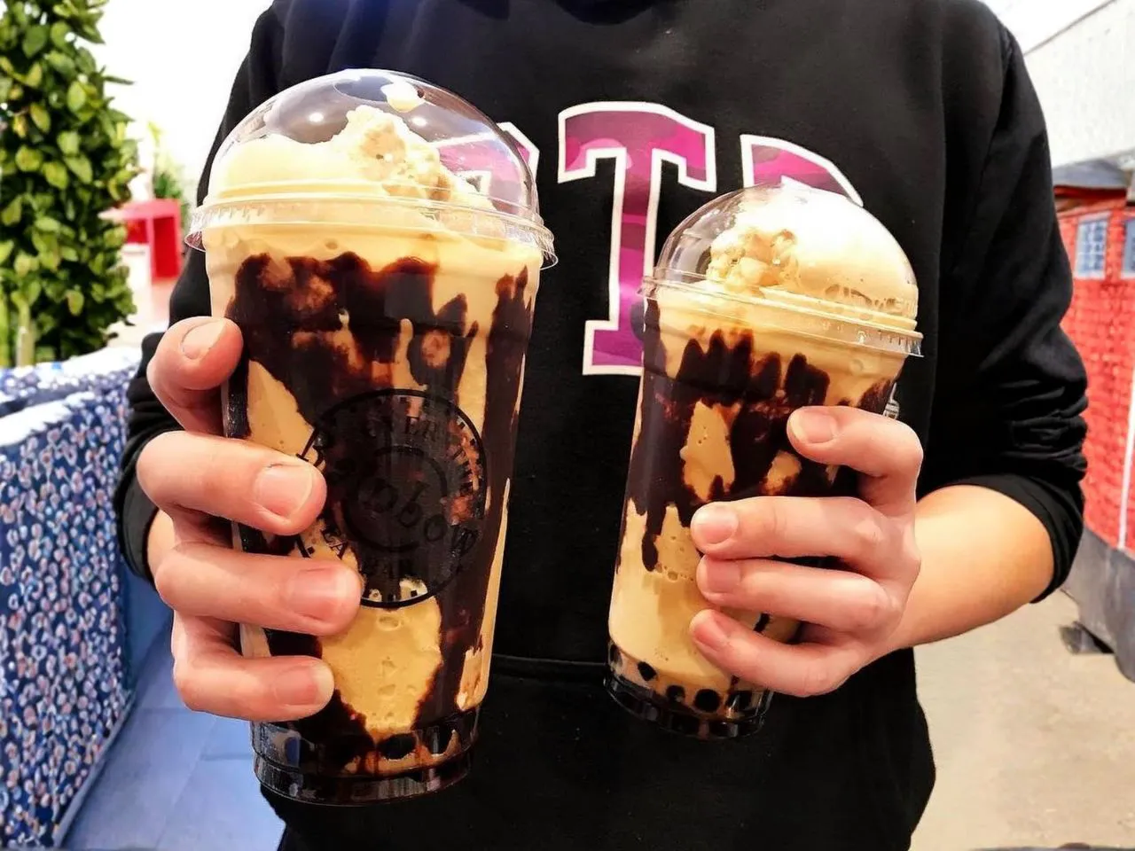 Two chocolate drizzled milk bubble tea cups held in a customer’s hands at Over The Rainbow Tea Bar, a Tea House in Renton
