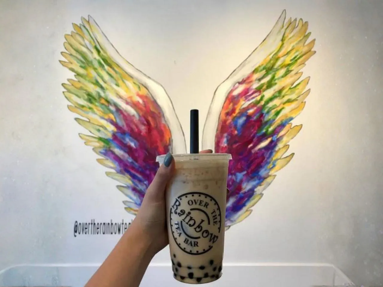 Classic milk bubble tea cup photographed in front of rainbow wing wall mural at Over The Rainbow Tea Bar, a Tea House in Renton